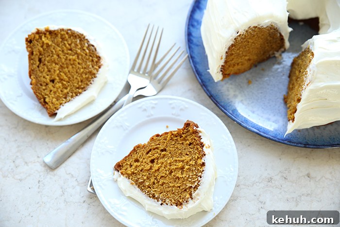 Pumpkin Bundt Cake with Cream Cheese Glaze — Fall Dessert Recipe 3 Two slices of pumpkin bundt cake with cream cheese frosting sitting on small plates with two forks crisscross on each other between the plates. In the upper right corner is a pumpkin bundt cake with cream cheese frosting on a round platter with a couple slices cut out.