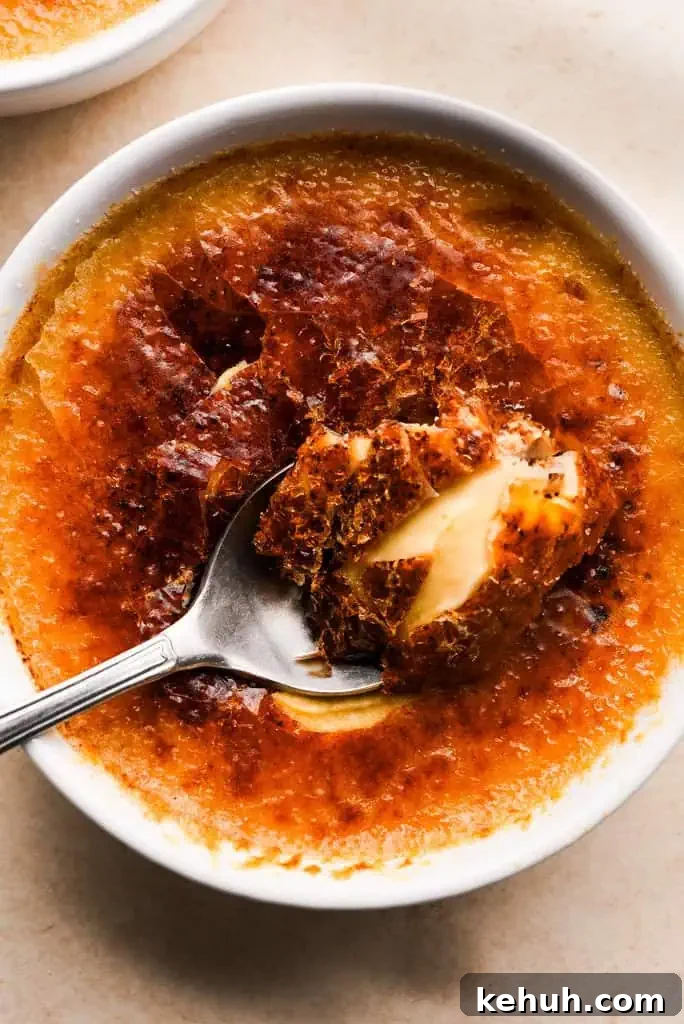 pumpkin spice creme brulee Close-up of a spoon lifting a bite of pumpkin creme brulee, showcasing the creamy texture beneath the crisp caramelized sugar.