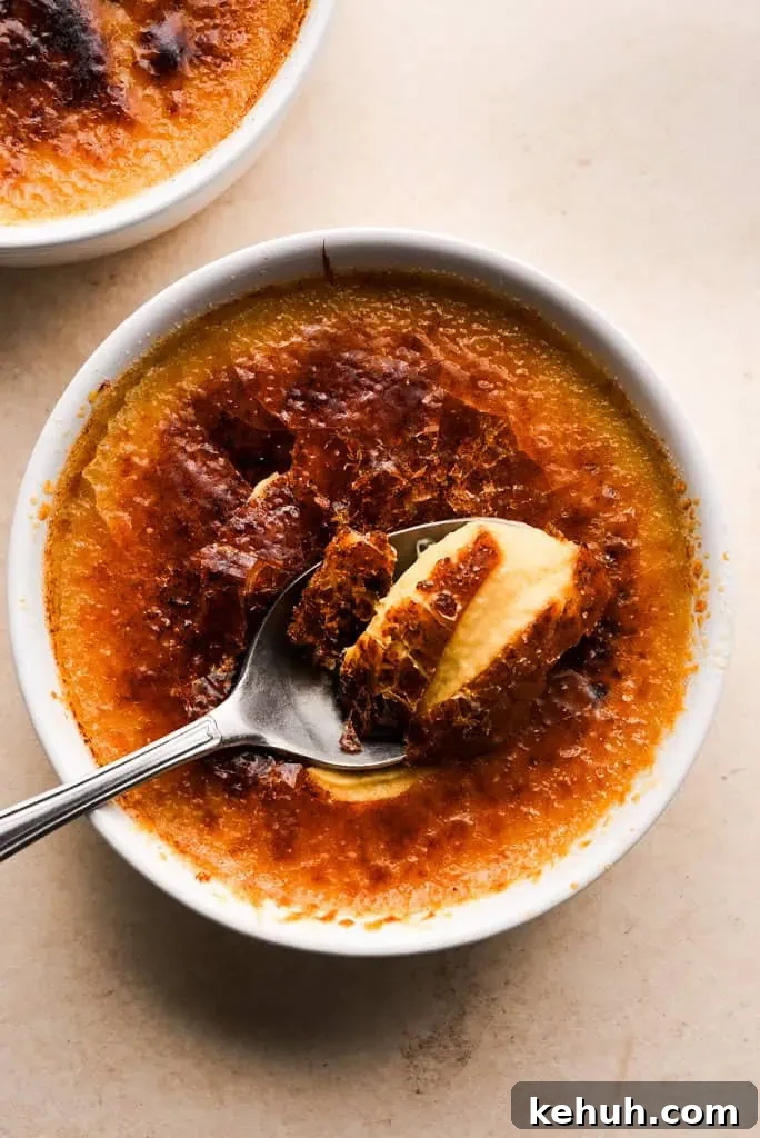 pumpkin creme brulee recipe Spoon breaking into the caramelized top of pumpkin creme brulee, revealing the smooth custard layer below.