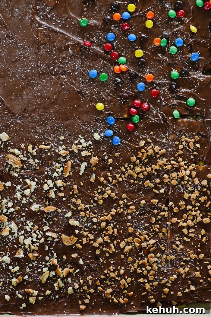 Classic Cracker Toffee Recipe with Crunchy Caramel Topping 8 Baking sheet is full of chocolate covered cracker toffee sprinkled with nuts, toffee and mini chocolate candies.