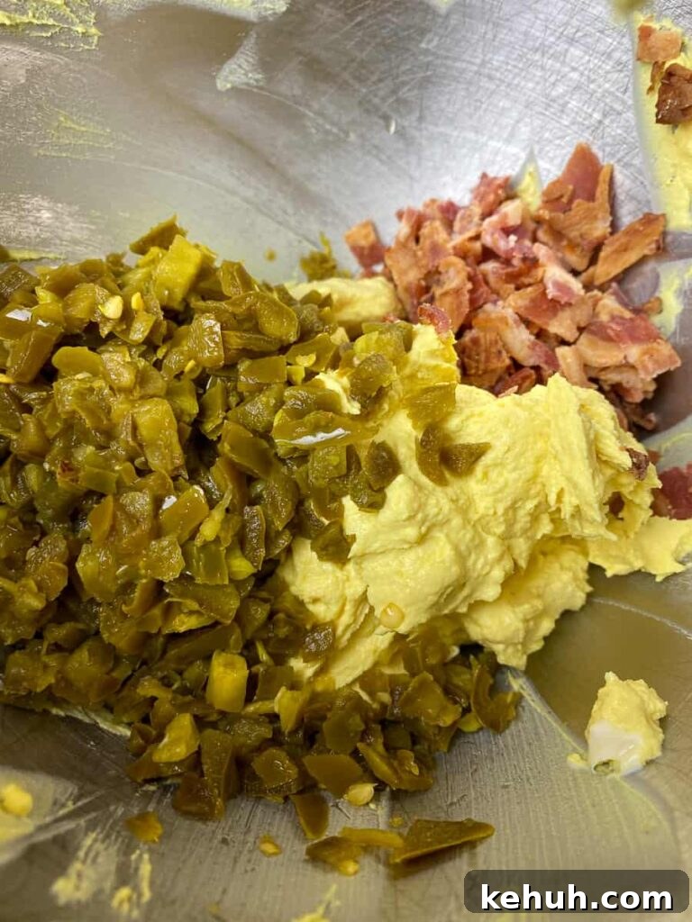 Bacon Jalapeño Deviled Eggs Recipe – Spicy Stuffed Egg Bites 7 Pickled jalapenos and bacon bits in mixing bowl with egg stuffing
