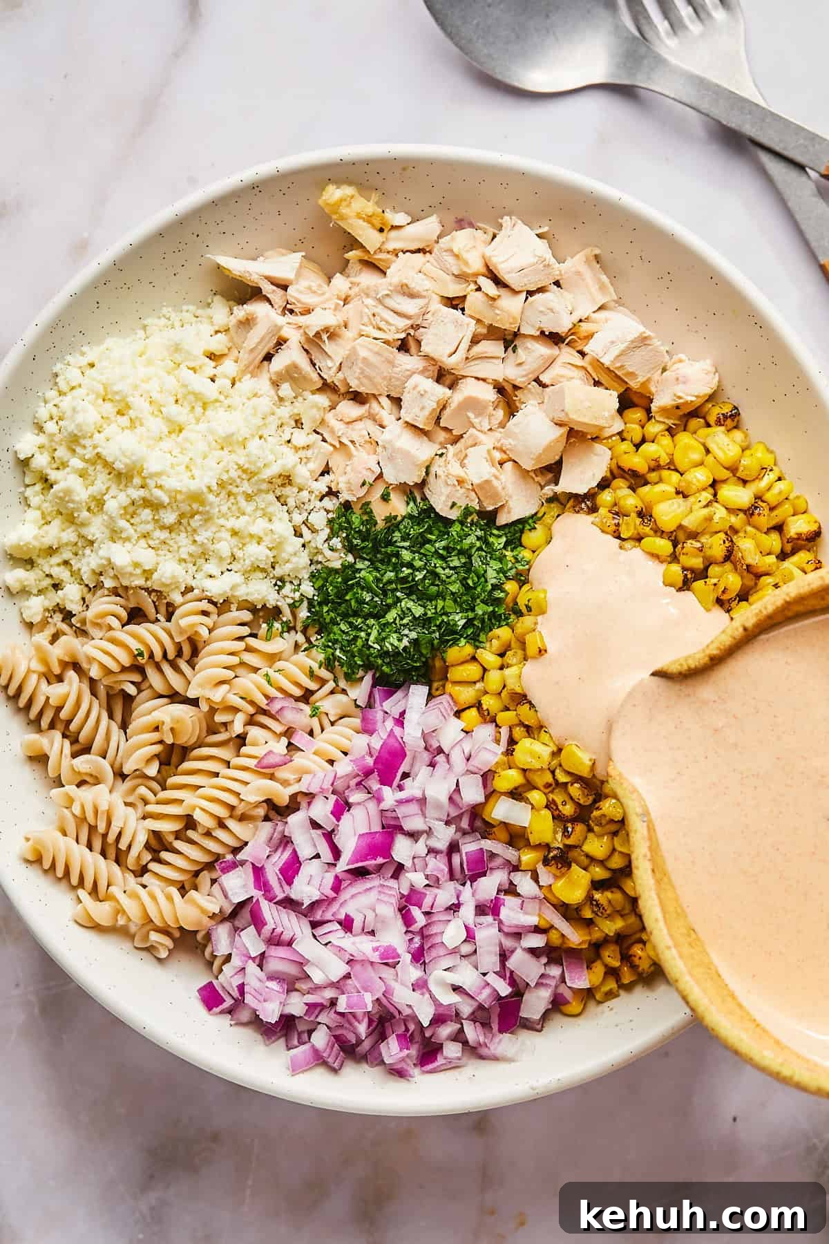 ingredients for street corn pasta salad in a large bowl with dressing being poured on top