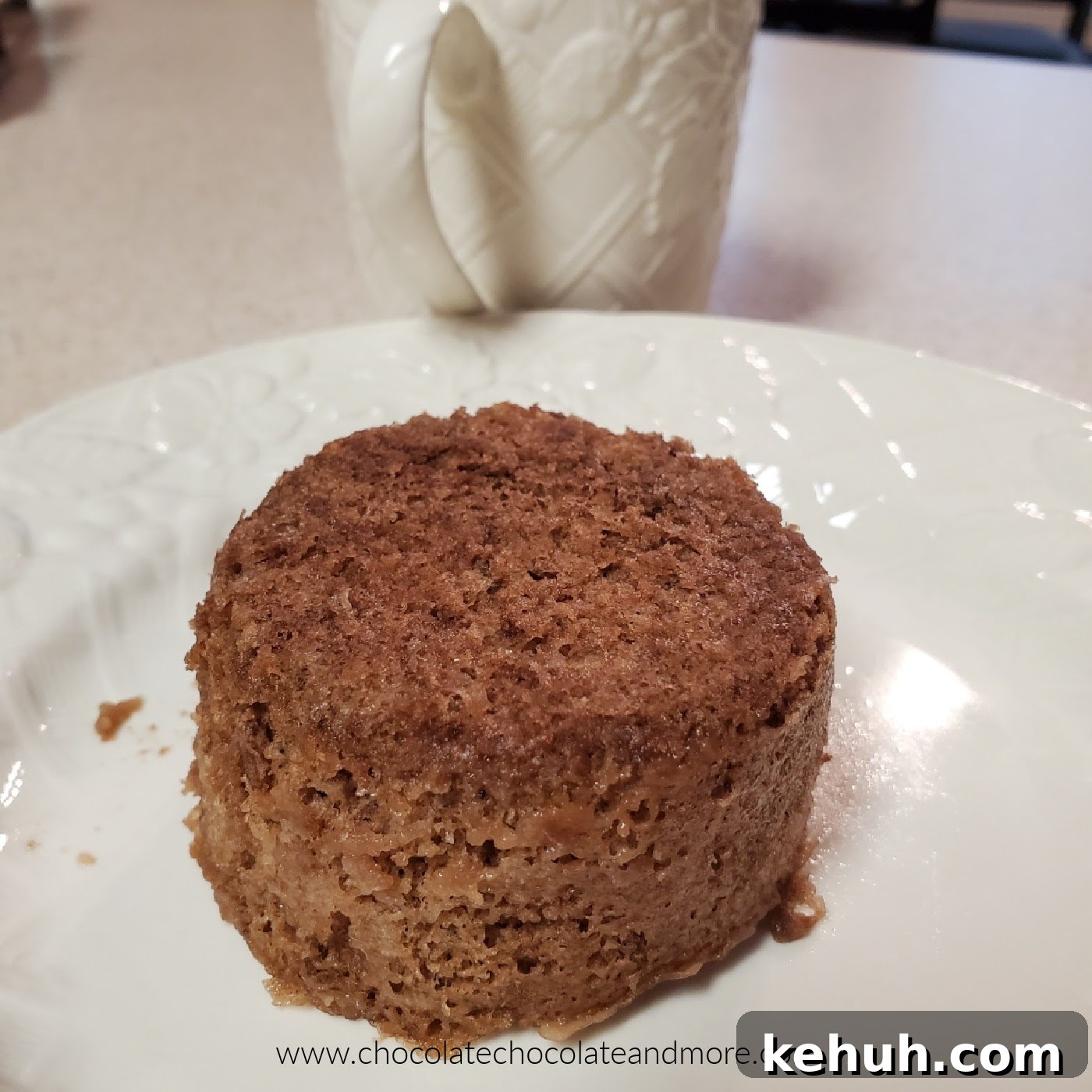 a small round chocolate cake on a plate with a mug in the background