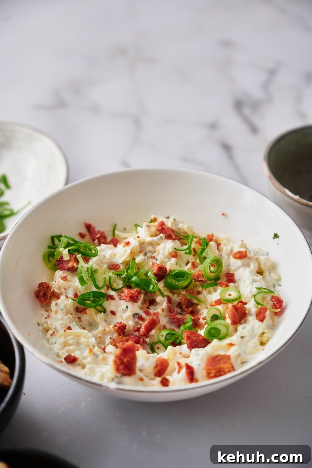 Ranch Bacon Cheddar Crack Dip Recipe for Parties 2 Crack dip in a white serving bowl topped with bacon bits and green onion.