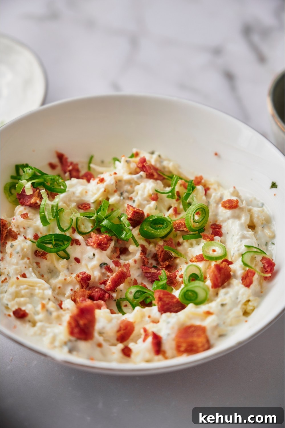 Ranch Bacon Cheddar Crack Dip Recipe for Parties 3 Crack dip in a white serving bowl topped with bacon and green onion.