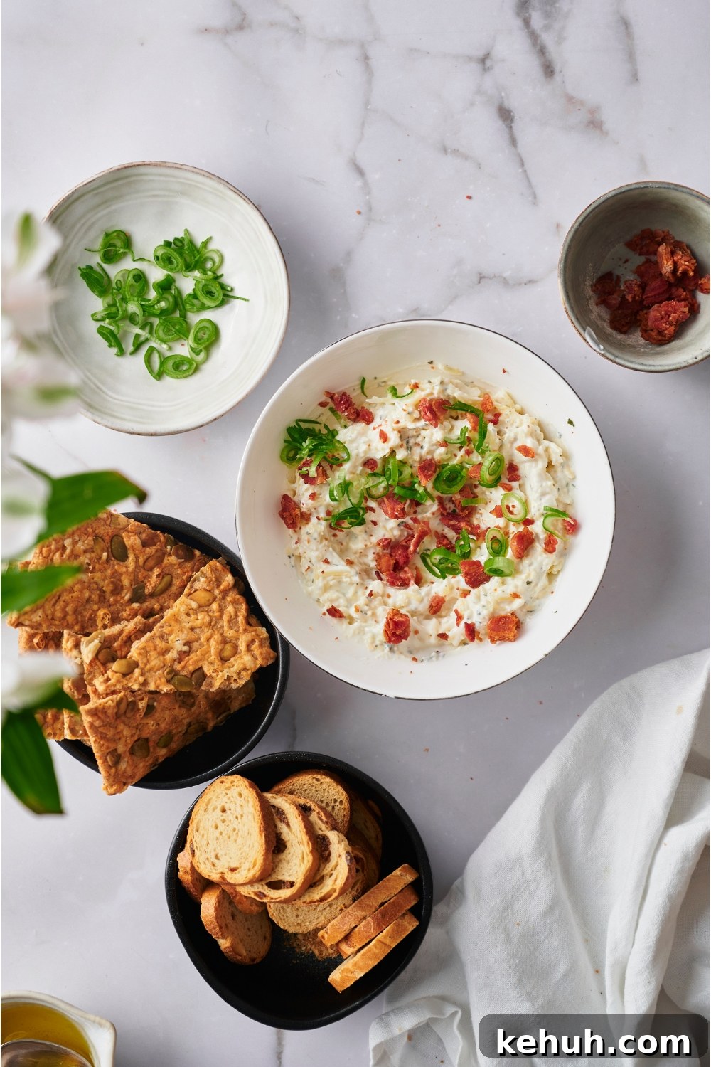 Ranch Bacon Cheddar Crack Dip Recipe for Parties 6 A bowl of crack dip garnished with bacon and diced green onion, surrounded by bowls of bread, crackers, bacon bits, and green onion.