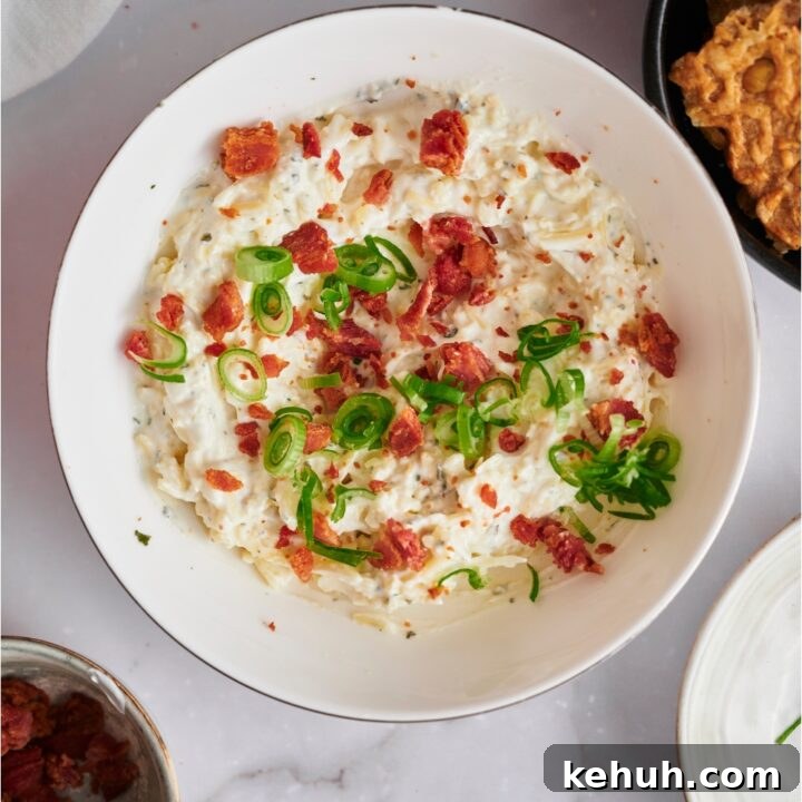 Crack dip in a white serving bowl topped with bacon and green onion.