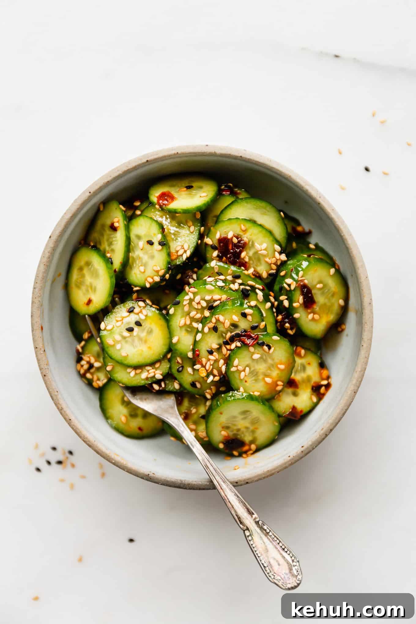 Quick Asian Cucumber Salad Ready in 10 Minutes 2 sliced cucumbers in a bowl topped with asian dressing and sesame seeds