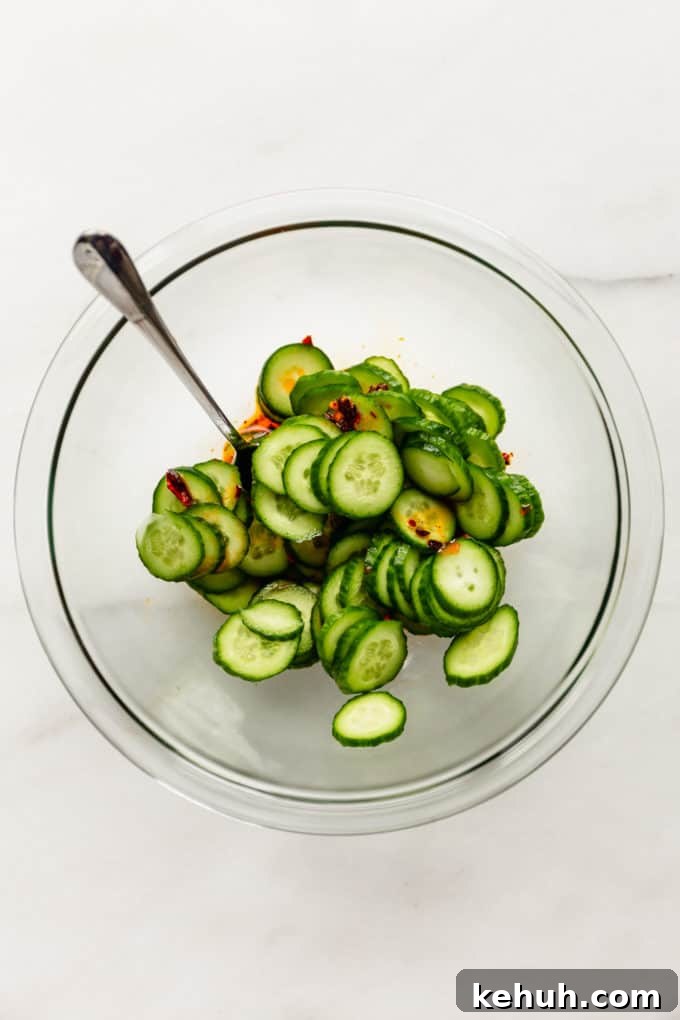 Quick Asian Cucumber Salad Ready in 10 Minutes 7 sliced cucumbers in a mixing bowl with dressing on the bottom