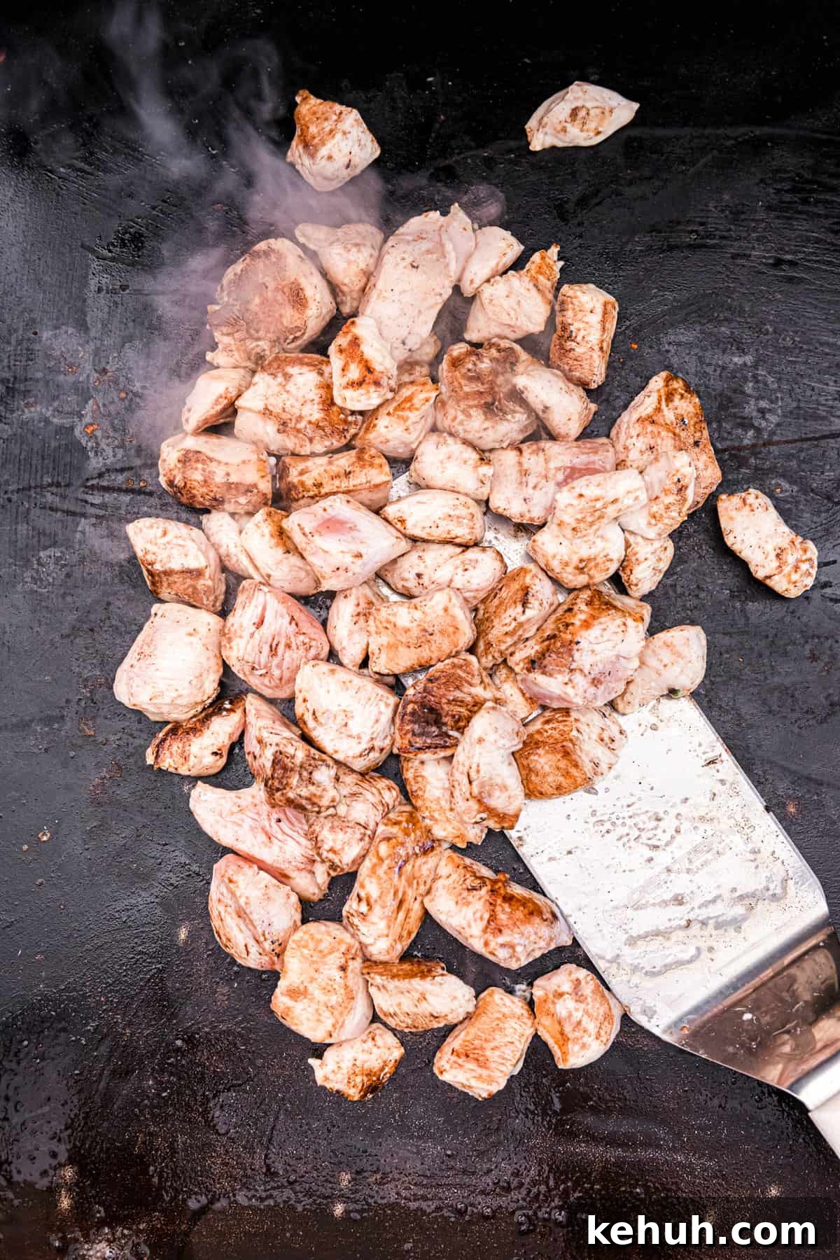 Coating the chicken cubes with teriyaki sauce on Blackstone for Teriyaki Chicken
