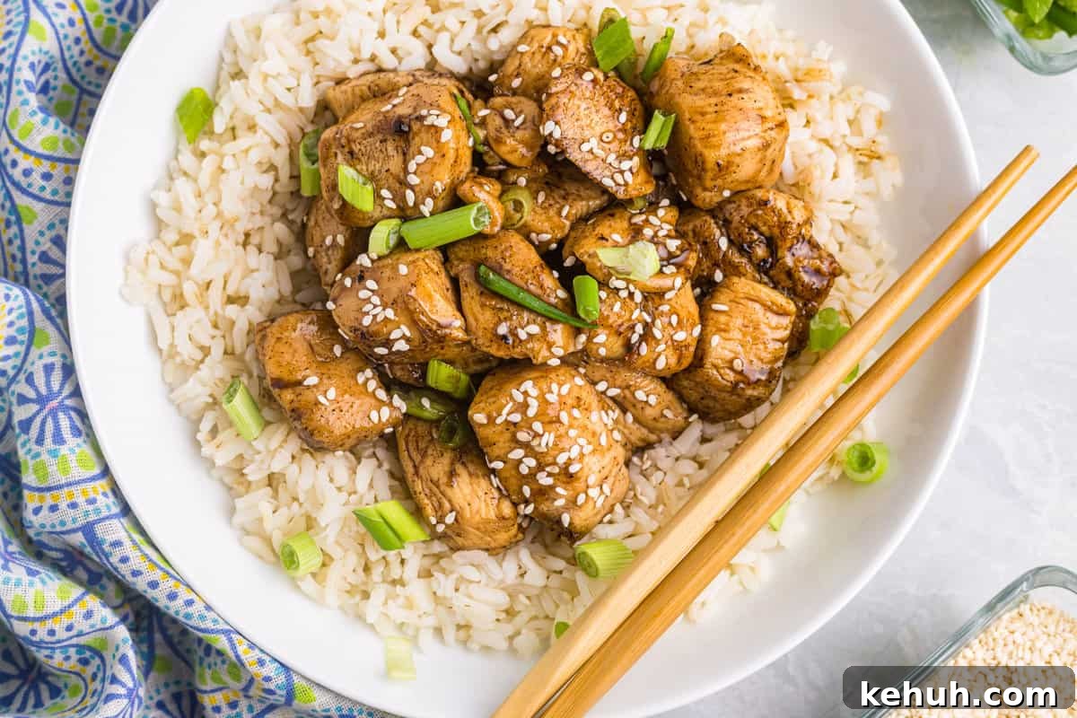 Teriyaki Chicken atop of a bed of rice in shallow bowl with chopsticks