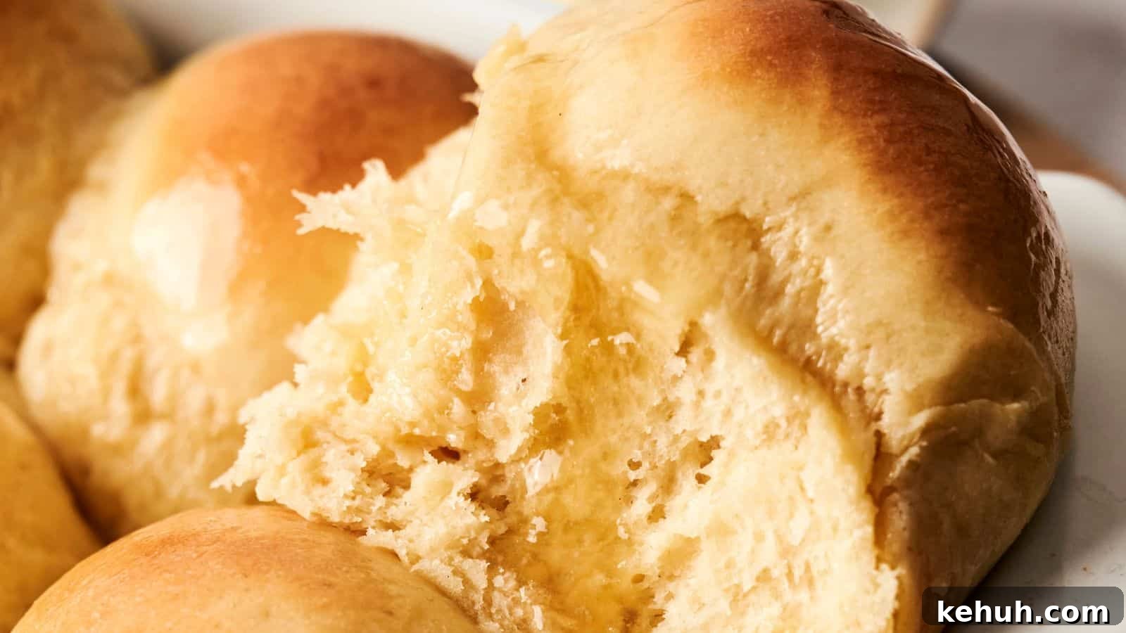 31 Homemade Thanksgiving Sides That Outshine Store-Bought 16 Close-up of freshly baked golden-brown dinner rolls, with one roll partially torn to show its soft, fluffy interior.