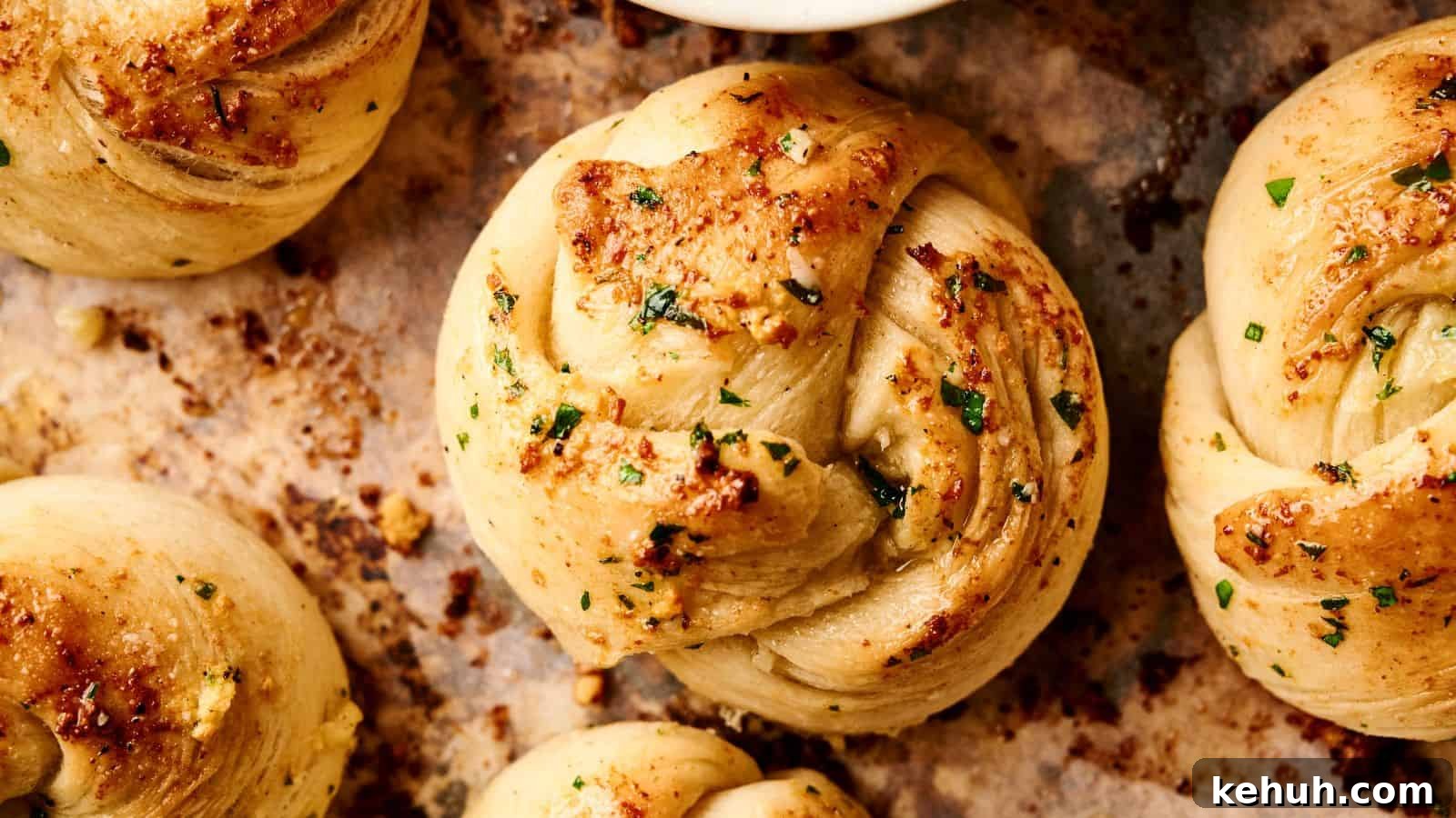 31 Homemade Thanksgiving Sides That Outshine Store-Bought 21 Close-up view of freshly baked garlic knots with parsley and seasoning, resting on a parchment-lined baking tray.
