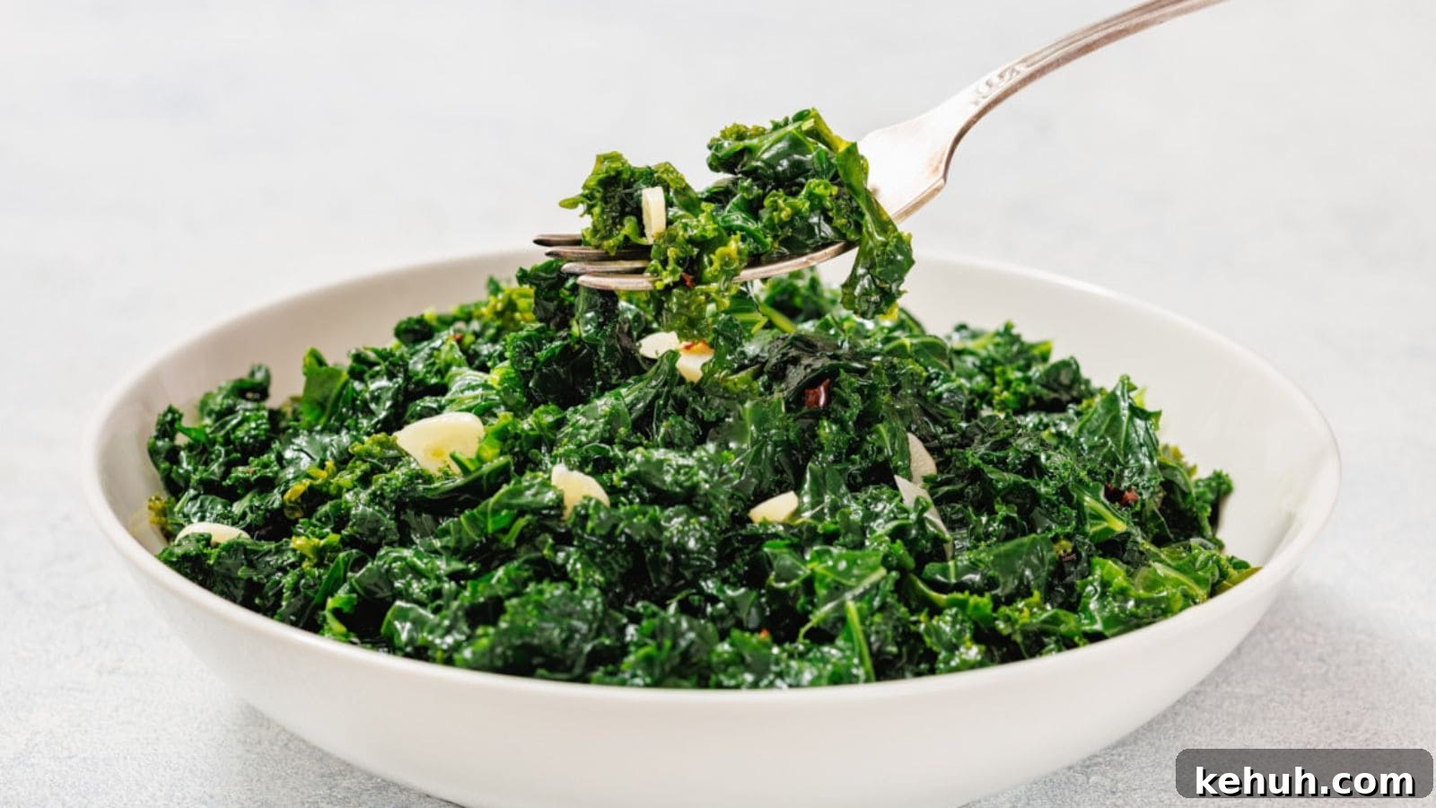 31 Homemade Thanksgiving Sides That Outshine Store-Bought 25 A white bowl filled with sautéed kale and sliced garlic, with a fork lifting a portion from the bowl.