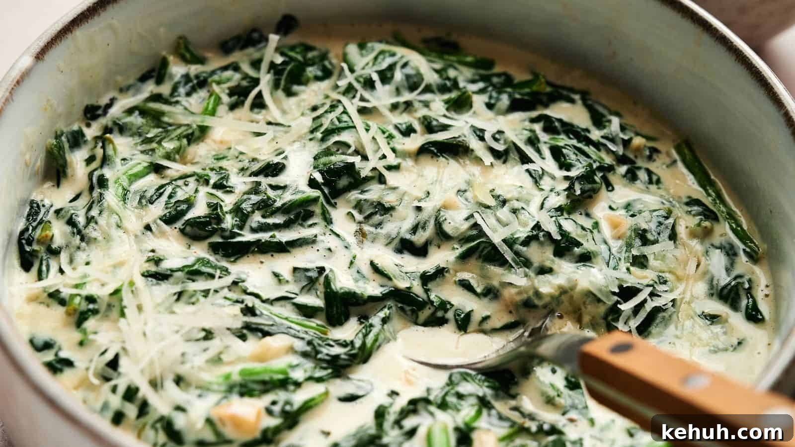 31 Homemade Thanksgiving Sides That Outshine Store-Bought 28 A bowl of creamy spinach topped with grated cheese, being stirred with a spoon.