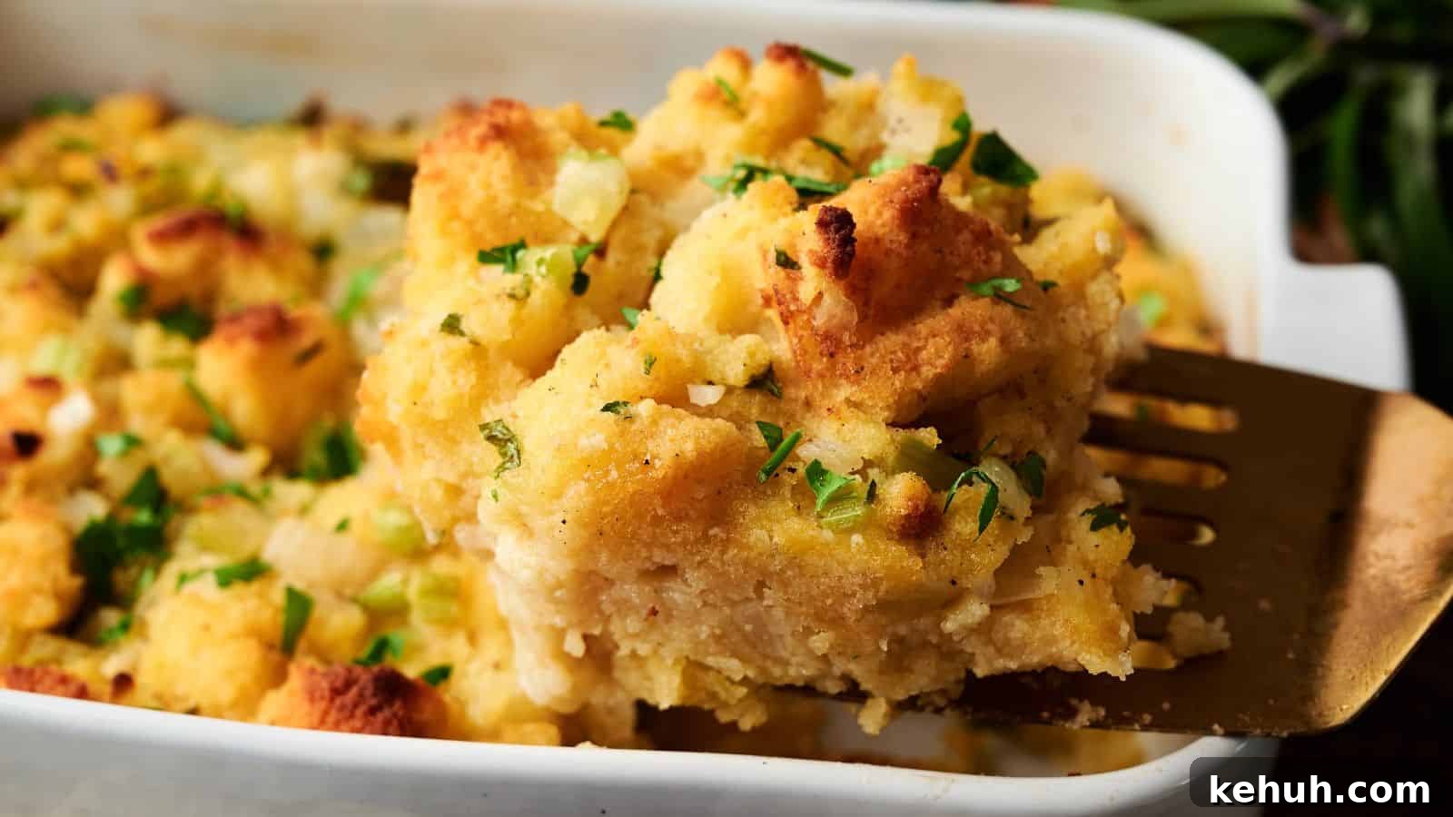 31 Homemade Thanksgiving Sides That Outshine Store-Bought 9 A metal spatula lifts a serving of baked stuffing topped with chopped parsley from a white casserole dish.