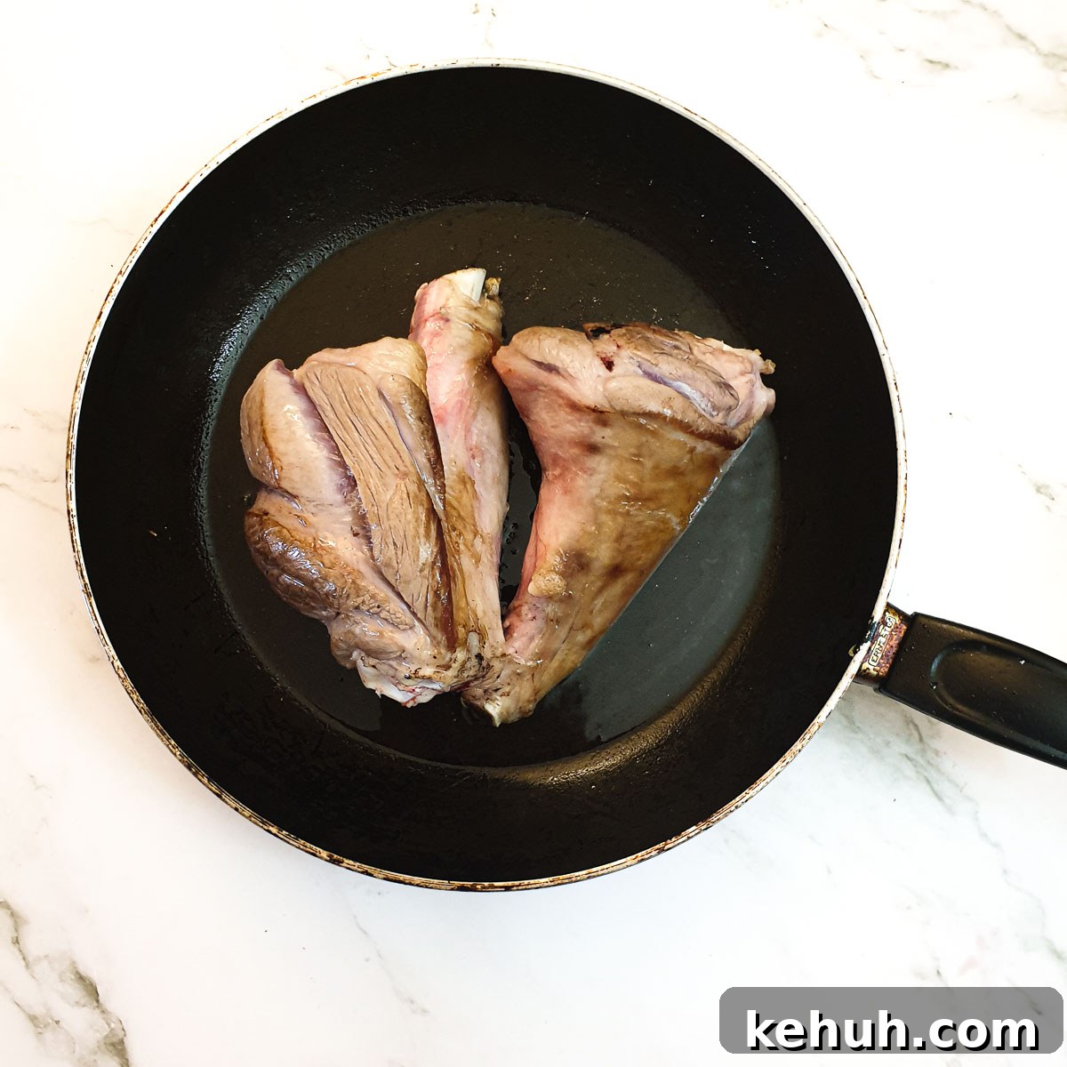 2 lamb shanks browning in a frying pan.