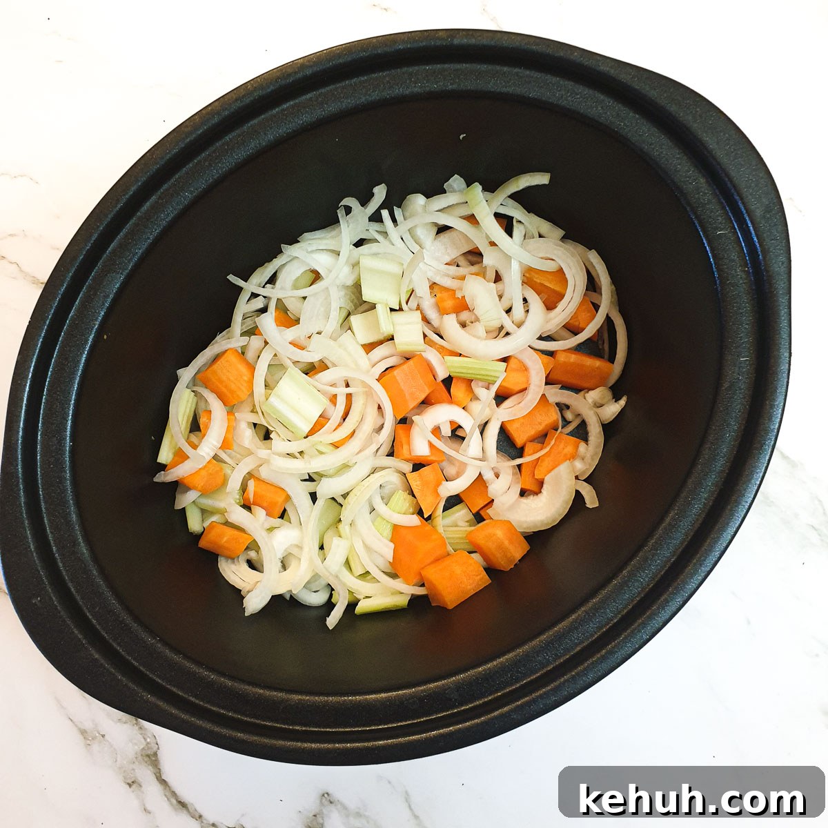 Sliced onions, carrots and celery in a slow-cooker.