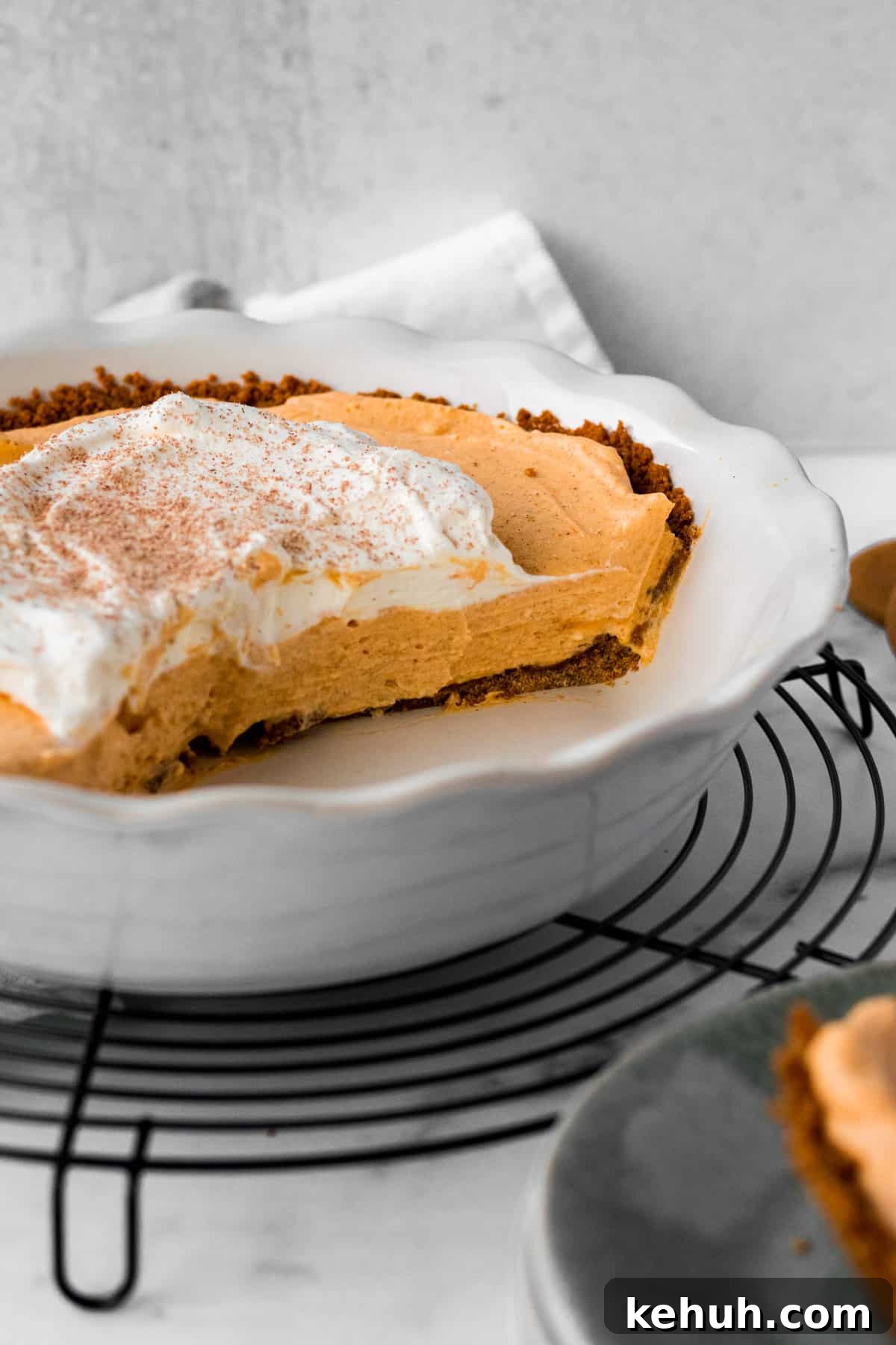Pumpkin Mousse Pie with Gingersnap Crust — Creamy Fall Dessert 3 white pie dish on circular cooling rack with half a pumpkin mousse pie inside