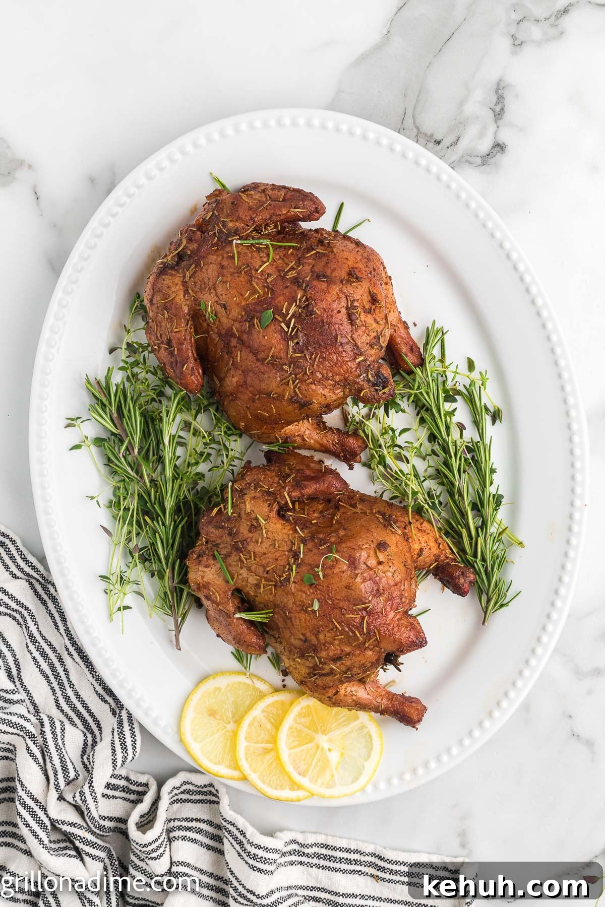 Smoked Cornish Hens Recipe: Juicy, Flavorful Whole Birds 7 Two Cornish Hens on a white platter with sprigs of Rosemary and slice lemons