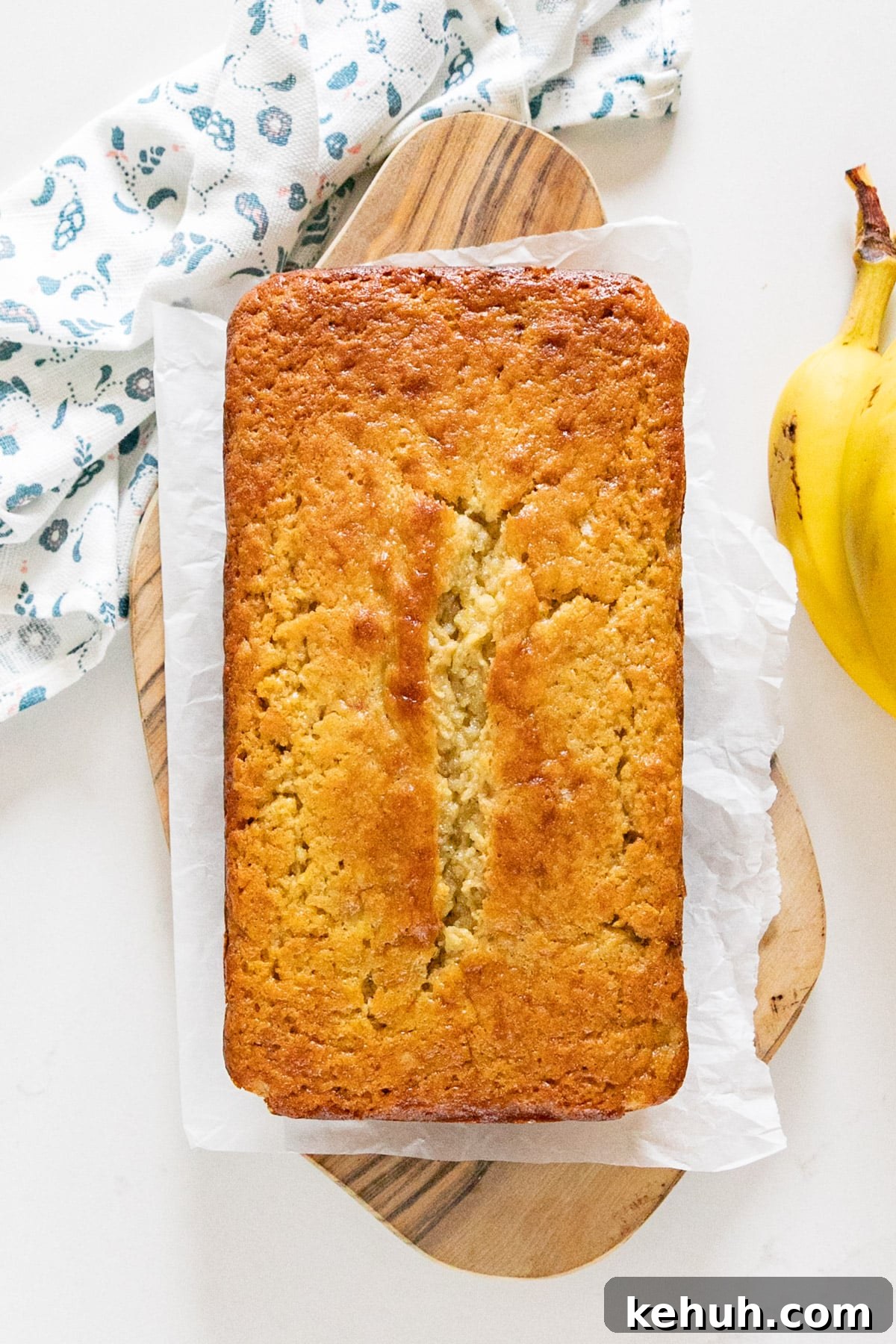 Moist Buttermilk Banana Bread with Brown Sugar Glaze 3 An overhead image of a loaf of banana bread on a cutting board with a napkin and a banana next to it.