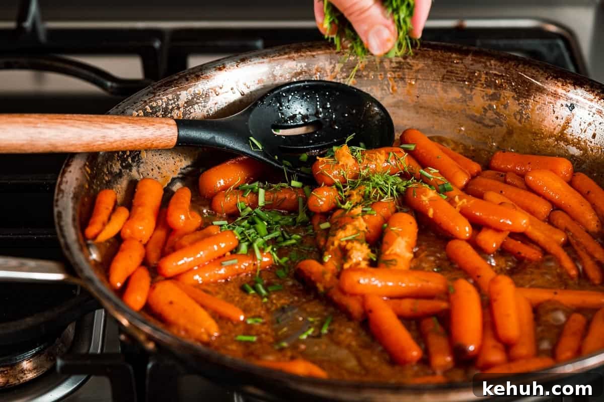 fresh herbs being sprinkled overtop pan of honey orange glazed carrots