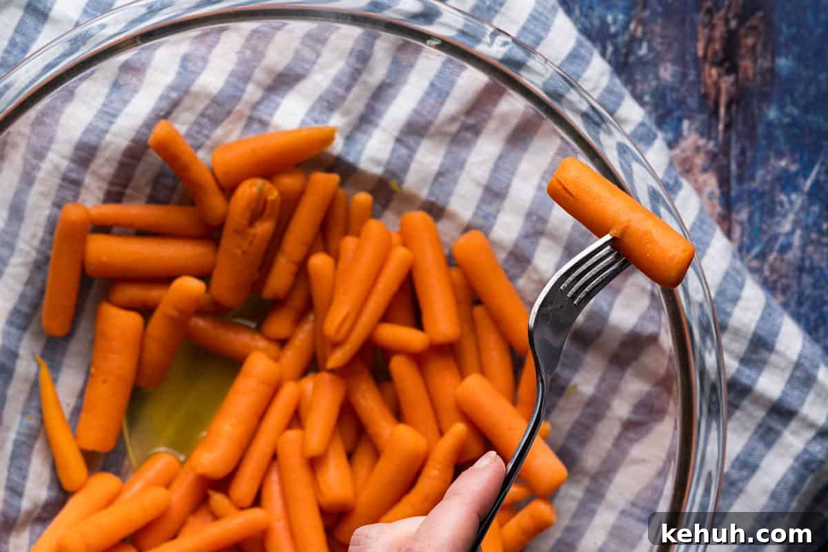 fork piercing cooked baby carrot overtop bowl of carrots