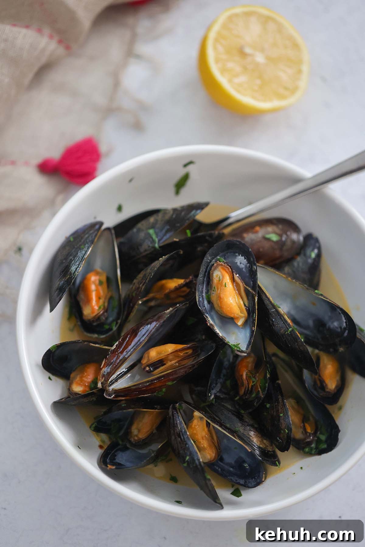 Mussels in Rich Lobster Broth: Savory Seafood Stew Recipe 2 black opened mussels with a spoon in a white bowl with a lemon on the side.