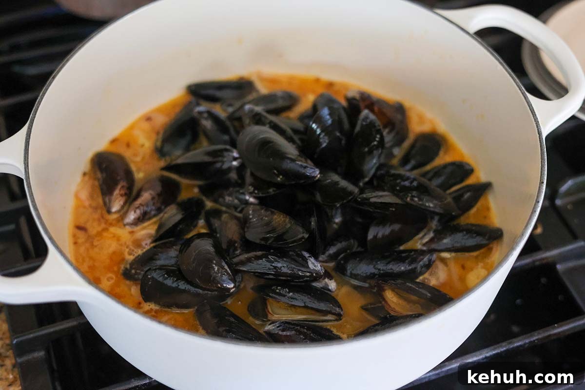 Mussels in Rich Lobster Broth: Savory Seafood Stew Recipe 5 black mussels and broth in a white pot.