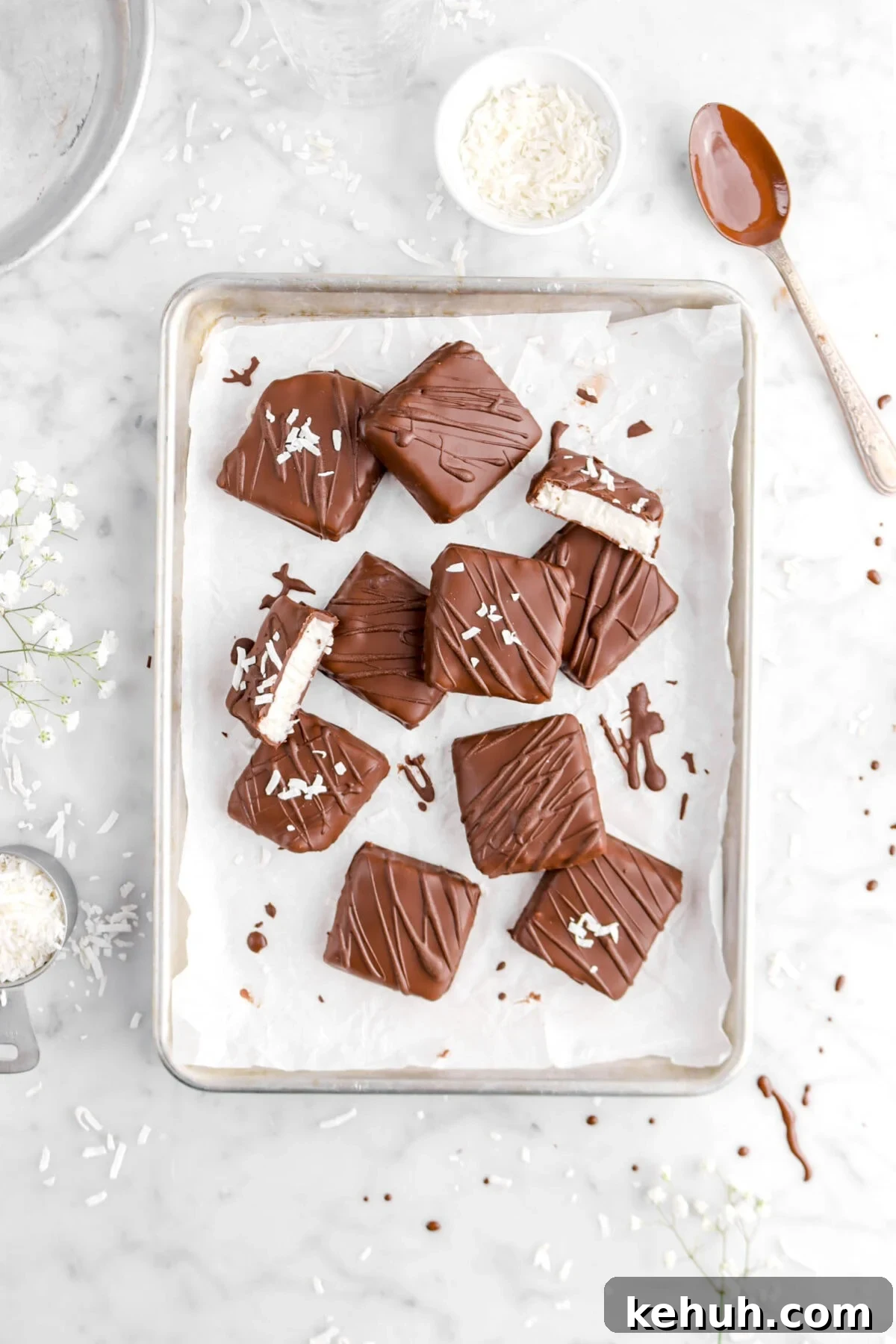 Coconut Cream-Filled Chocolate Truffles: Decadent Homemade Recipe 2 overhead shot of ten coconut filled chocolates with one cut in half, bowls of flaked coconut around, and spoonful of melted chocolate on marble surface