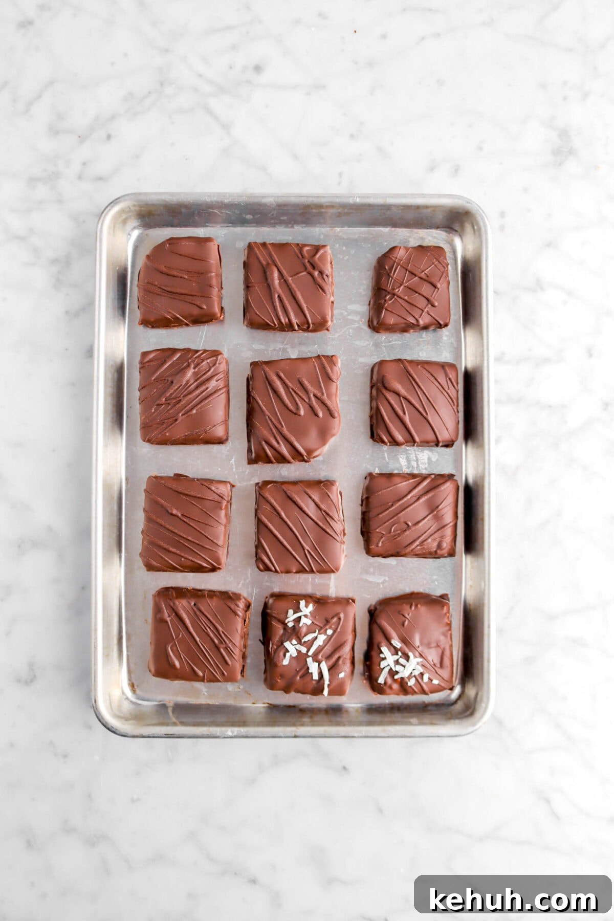 Coconut Cream-Filled Chocolate Truffles: Decadent Homemade Recipe 17 twelve square chocolates on small sheet pan with coconut flakes on two chocolates