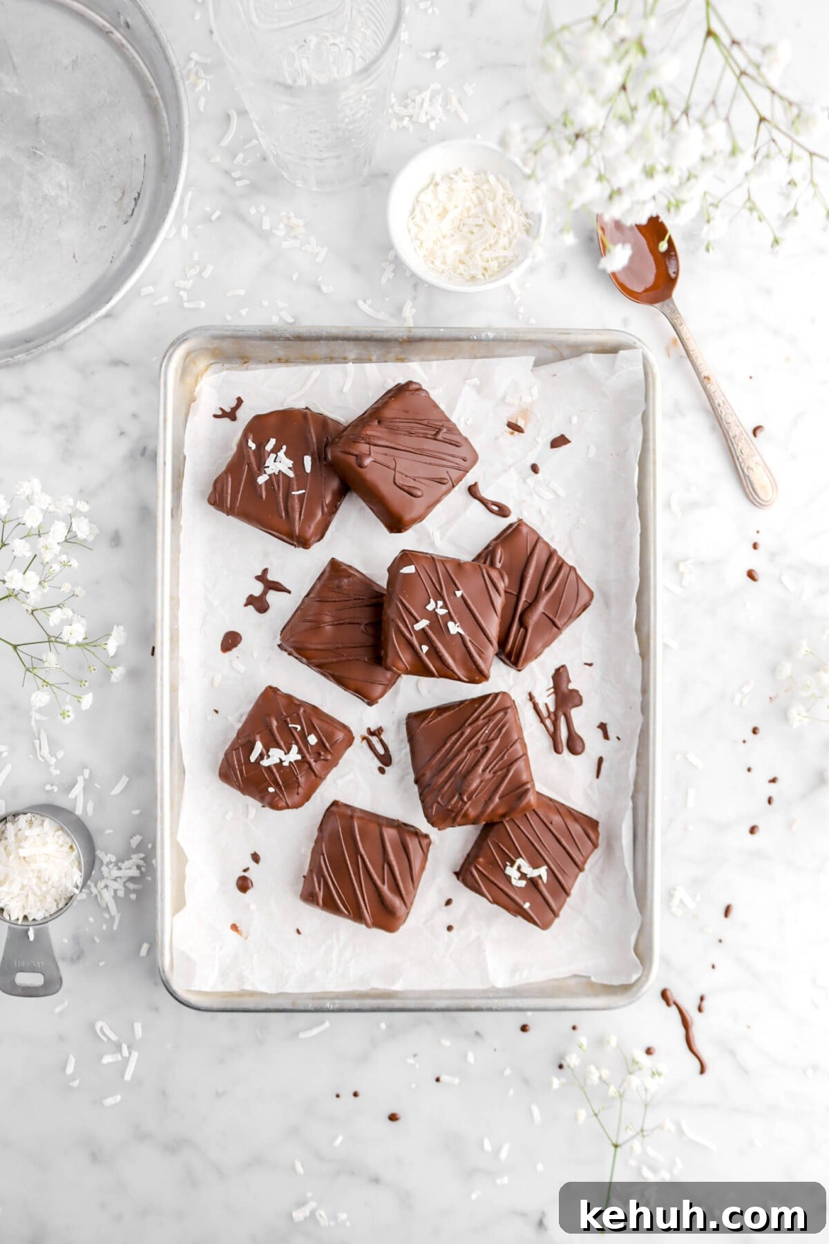 Coconut Cream-Filled Chocolate Truffles: Decadent Homemade Recipe 5 chocolate squares on parchment lined sheet pan with coconut flakes around and spoonful of melted chocolate