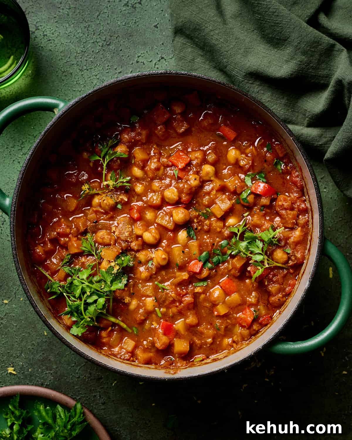 vegan tagine with chickpeas in a green dutch oven, garnished with parsley, on a green table.