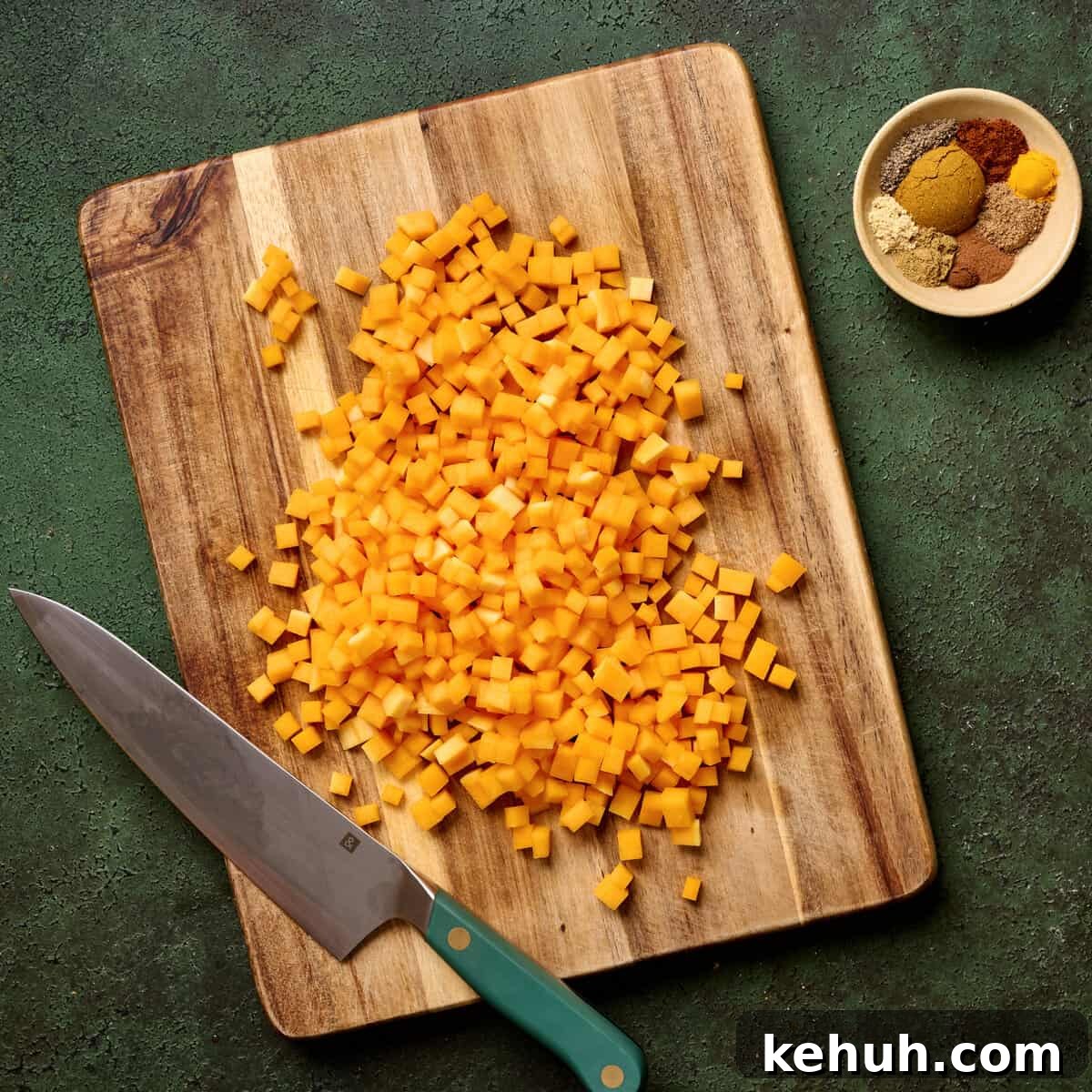Small chopped butternut squash pieces on a wooden cutting board with a knife.