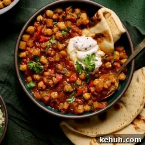 bowl of vegan tagine with chickpeas topped with yogurt and pita on a green table with green glasses.