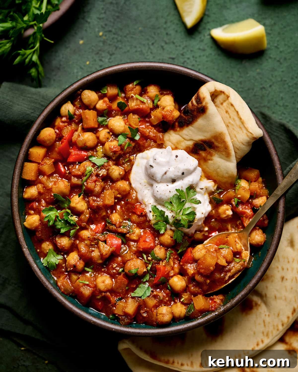 Close up of bowl of tagine with pita and yogurt on a dark green table.