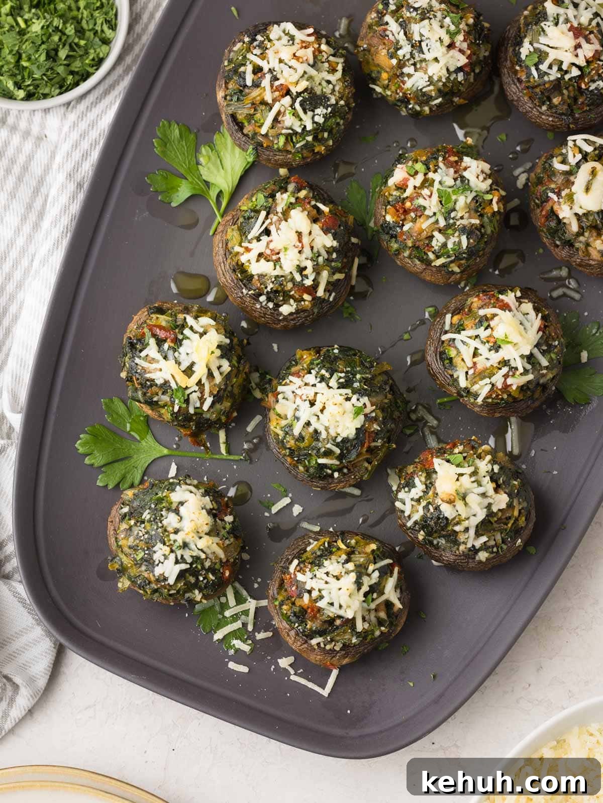 Parmesan Spinach-Stuffed Mushrooms: Savory Appetizer Recipe 2 Spinach stuffed mushrooms with sun-dried tomatoes, herbs, and parmesan cheese on a gray platter.