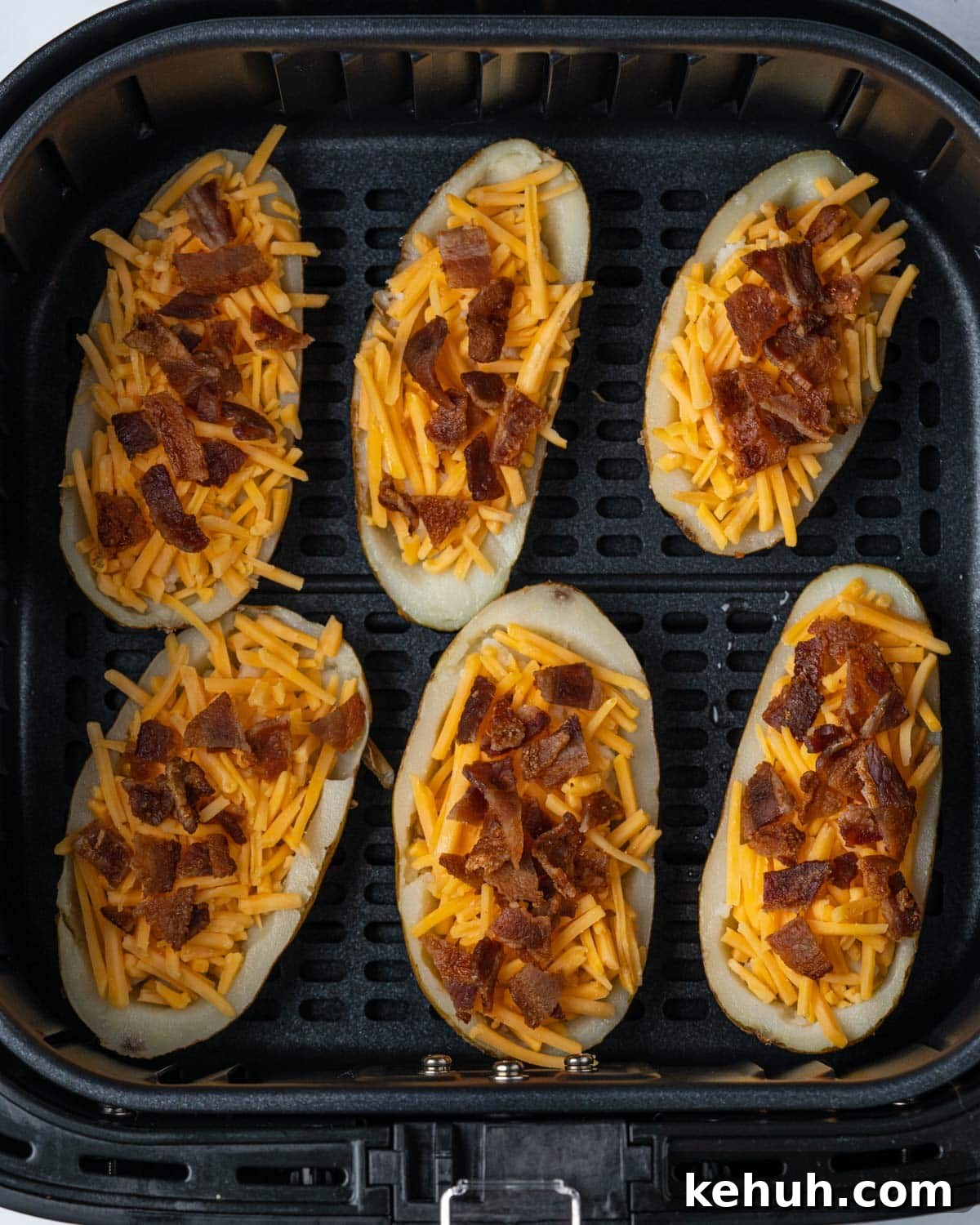 Crispy Air Fryer Potato Skins Filled with Cheesy Bacon 7 uncooked potato skins in air fryer basket.