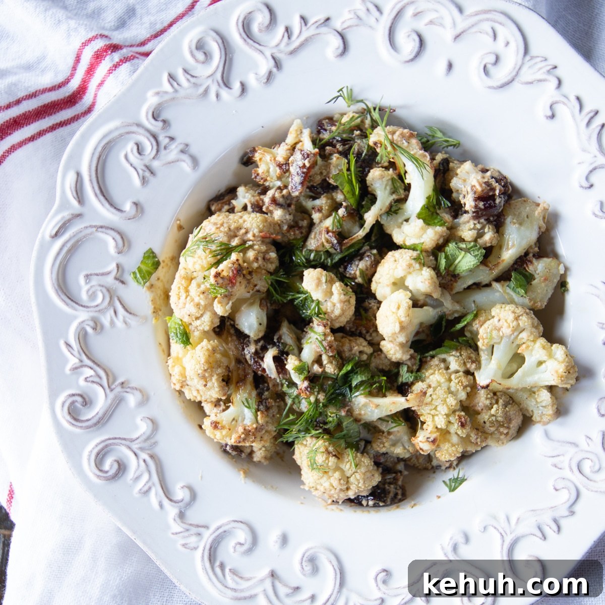 Roasted Cauliflower with Tahini Sauce and Sweet Dates 5 Roasted cauliflower tossed in a tahini sauce with dates, topped with mint and dill in a serving bowl.