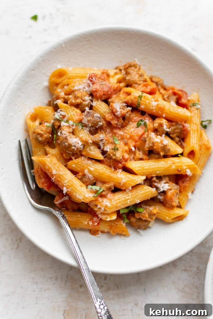 spicy Italian sausage penne pasta with a fork in a white bowl