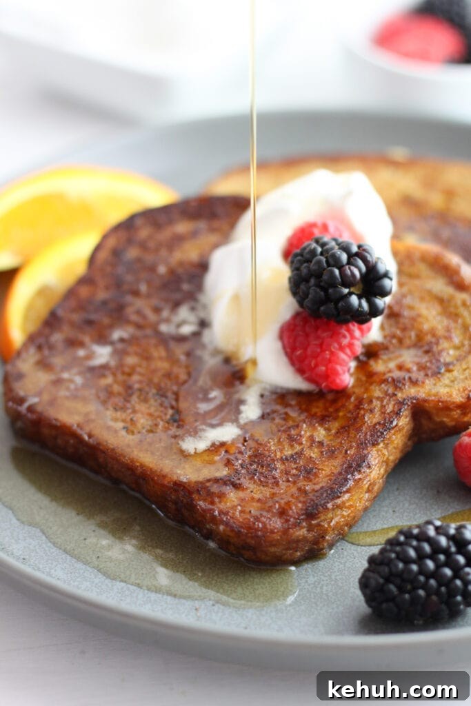 Brioche French Toast Casserole Recipe for Brunch and Holidays 14 A gray plate with two slices of brown sugar french toast with whipped cream and berries and maple syrup being poured on top.