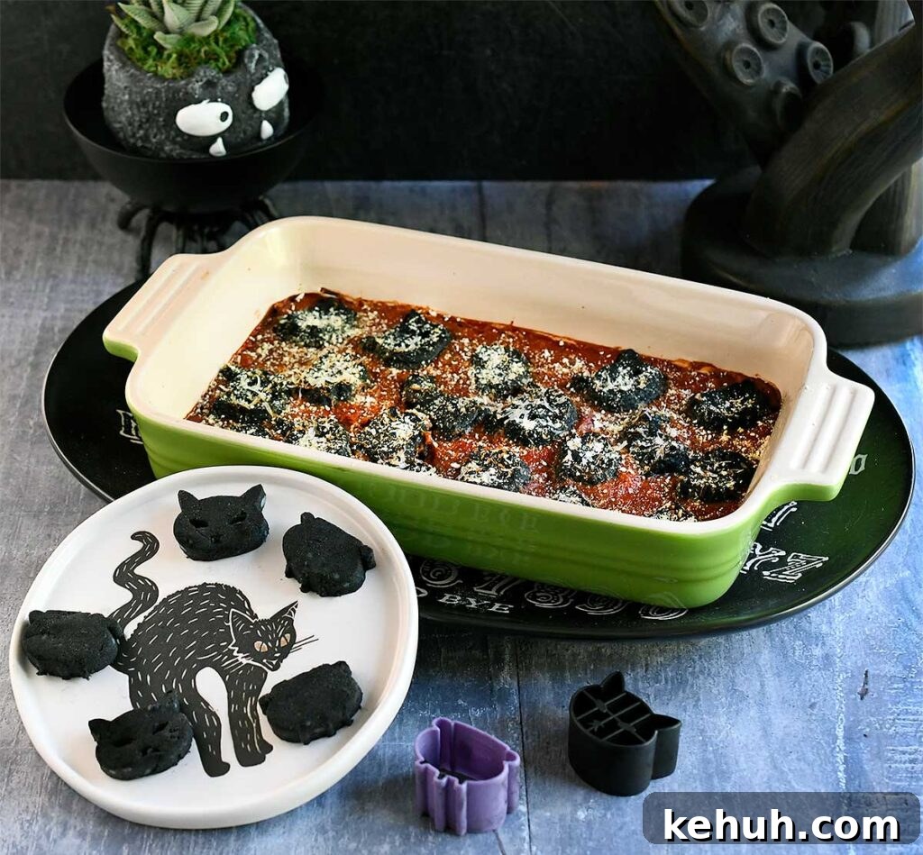 Black vegan gnocchi cut out into cat and cauldron shapes baked in a tomato sauce with spooky Halloween decorations.