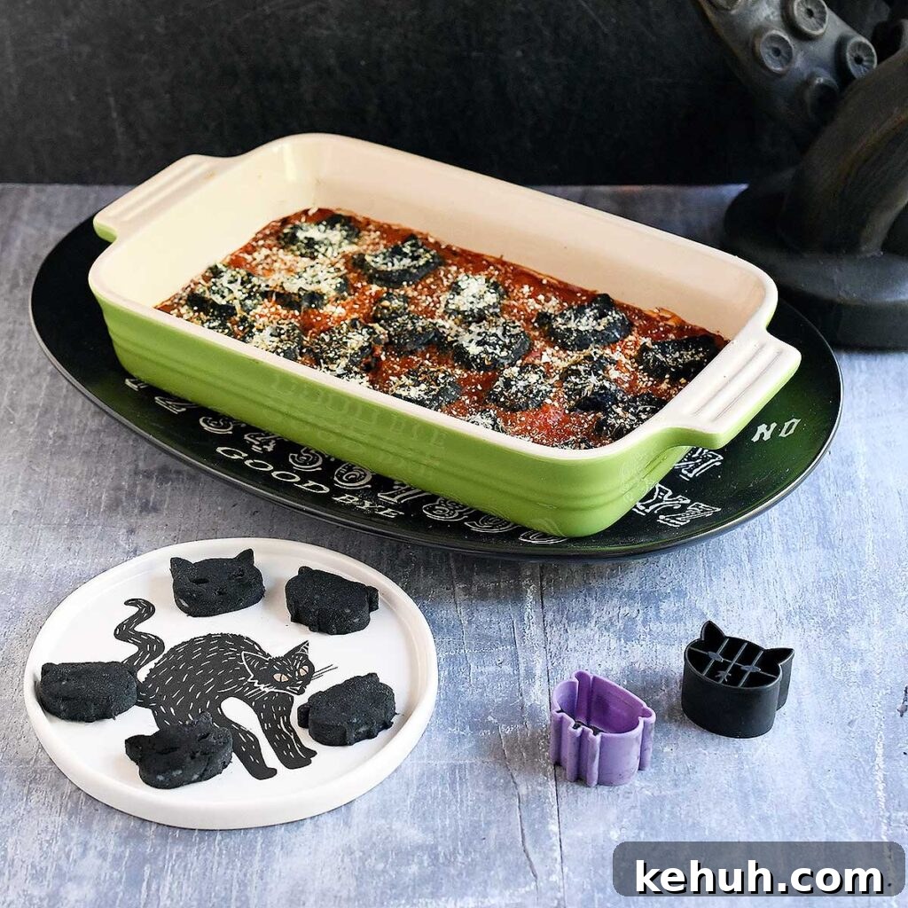 Black vegan gnocchi cut out into cat and cauldron shapes baked in a tomato sauce with spooky Halloween decorations.