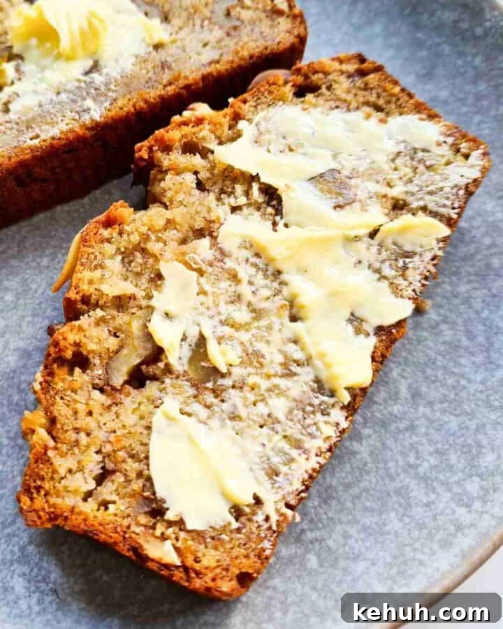 Close up of a slice of banana bread on a grey plate with a generous amount of butter