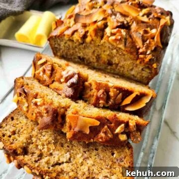 A loaf of banana bread with half of it thickly sliced on a glass plate