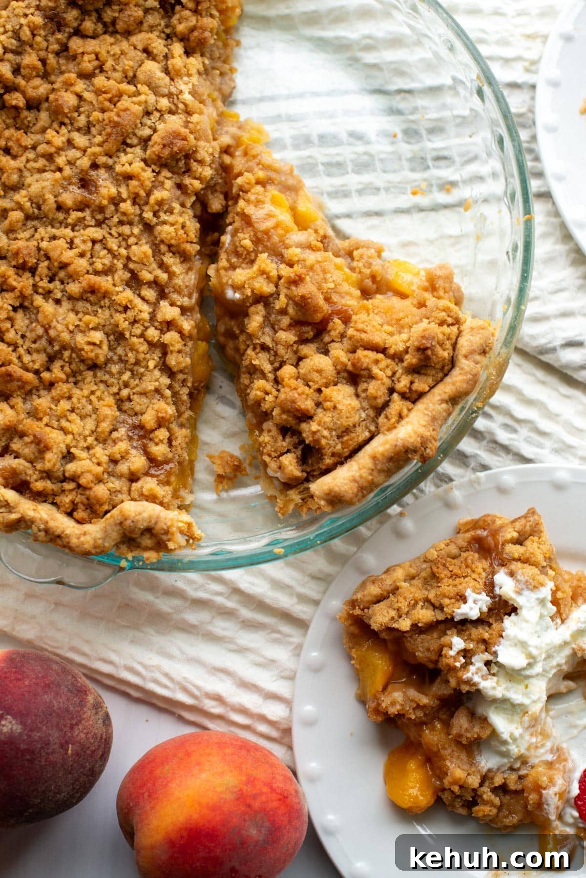 Sourdough Peach Crumb Pie Recipe with Flaky Rustic Crust 13 A slice of peach pie sits on a plate with whipped cream on top next to the pie plate containing the majority of the peach pie.