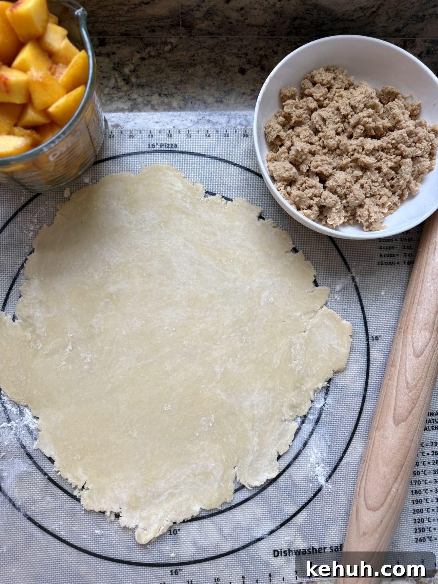 Sourdough Peach Crumb Pie Recipe with Flaky Rustic Crust 9 A pie crust is rolled out on a pastry mat next to a jar of peach filling and a bowl of crumb topping.