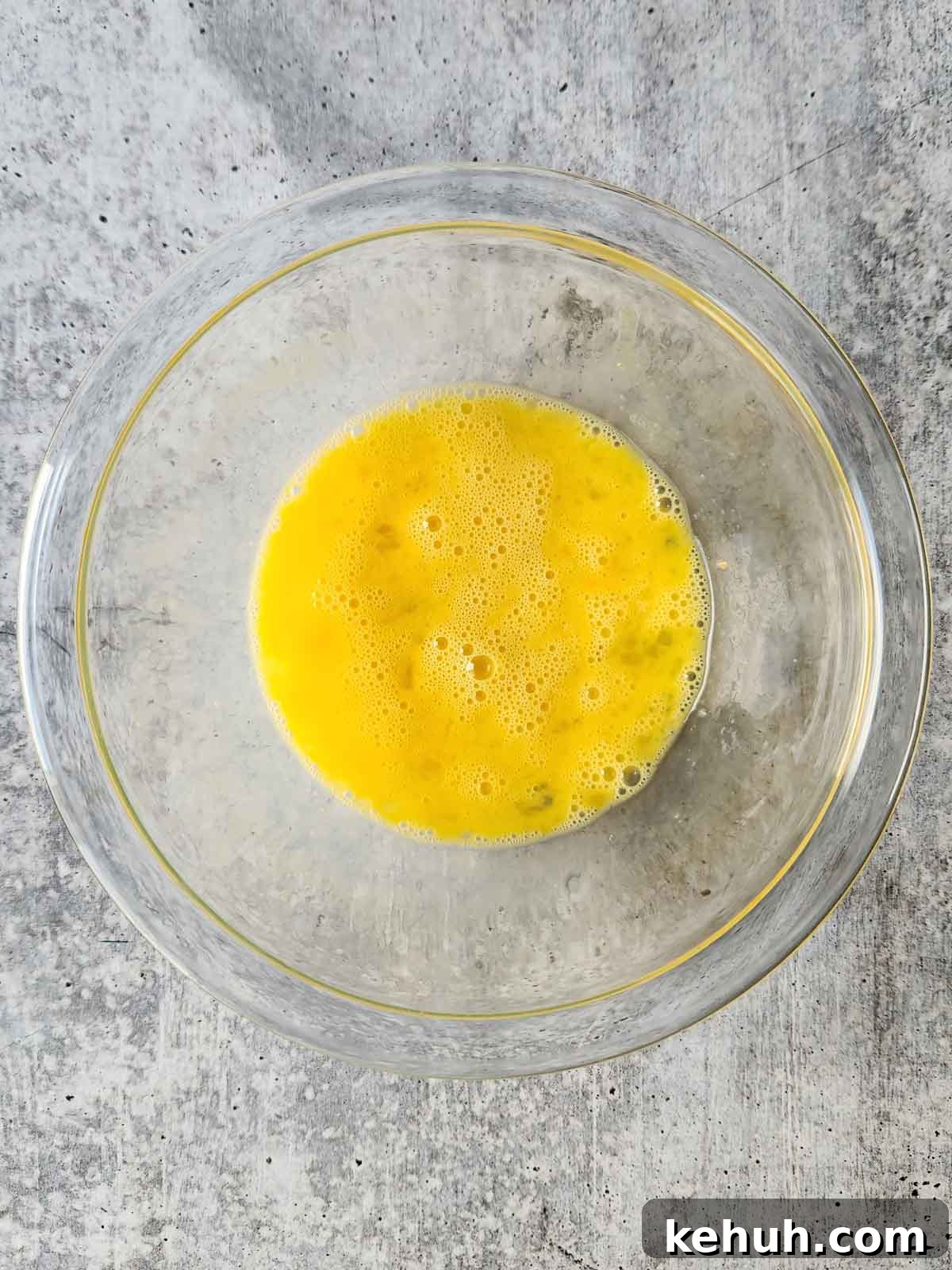 Creamy Goat Cheese Scrambled Eggs with Herbs and Cherry Tomatoes 4 Whisked eggs in a clear bowl.