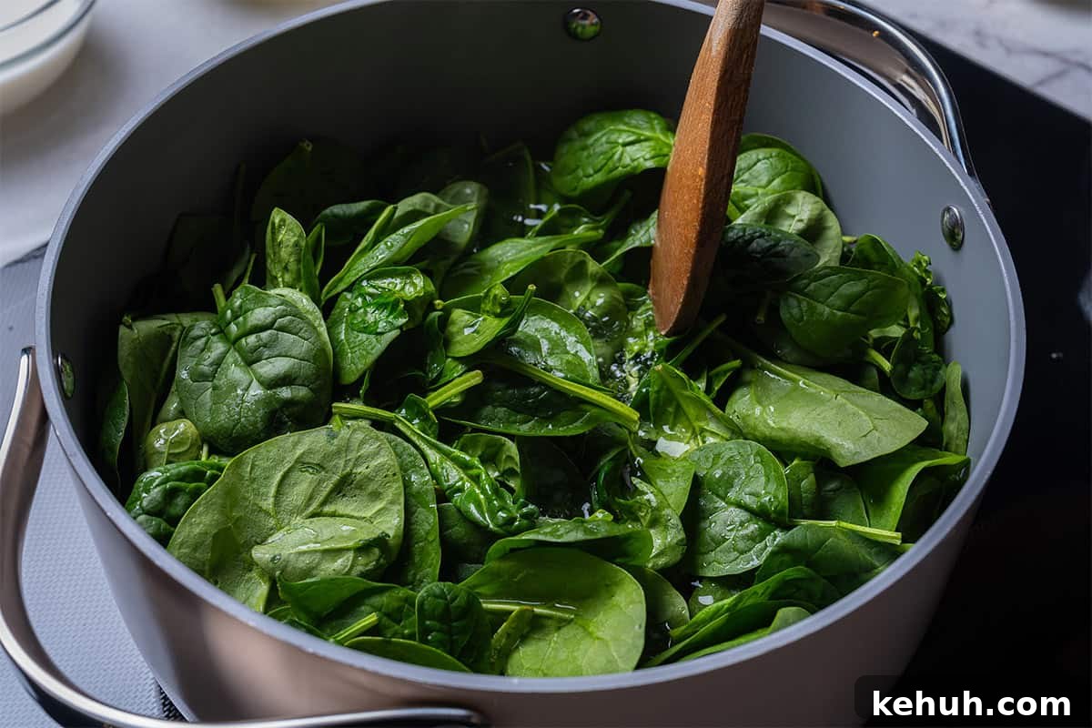 Creamy Parmesan Spinach Recipe — Quick Sautéed Side Dish 6 pot with spinach and a wooden spoon touching the top