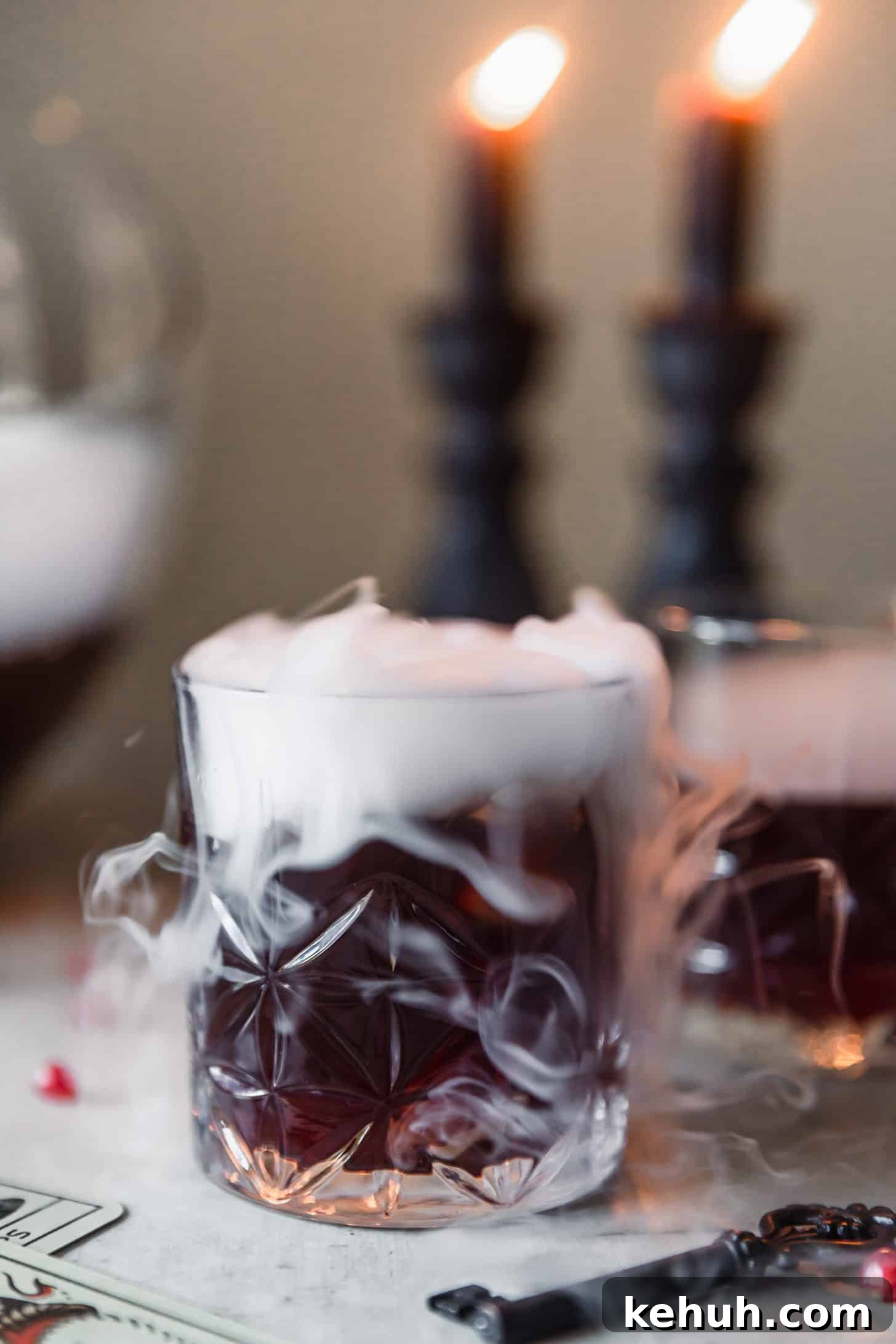 Spooky Witches Brew Punch Recipe for Halloween Parties 3 A closeup of a red-purple drink with smoke on a grey table next to vintage keys and cards.
